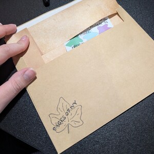 May include: A brown envelope with the text "PAGES OF IVY" and a leaf design. Inside, a card with the words "translate to a Flower!" is partially visible. The envelope is open, revealing the card.