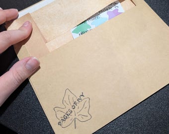 May include: A brown envelope with the text "PAGES OF IVY" and a leaf design. Inside, a card with the words "translate to a Flower!" is partially visible. The envelope is open, revealing the card.