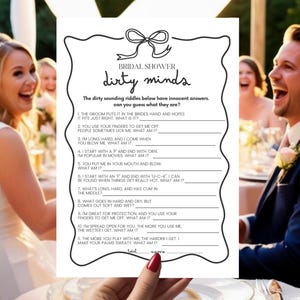 May include: A black and white "Bridal Shower Dirty Minds" game card with a bow illustration. The card features a list of riddles with blank spaces for answers. The image is held by a person with red nail polish, with a wedding party in the background.