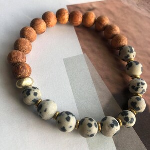 May include: A brown wooden beaded bracelet with a section of white and black speckled beads and gold spacers.