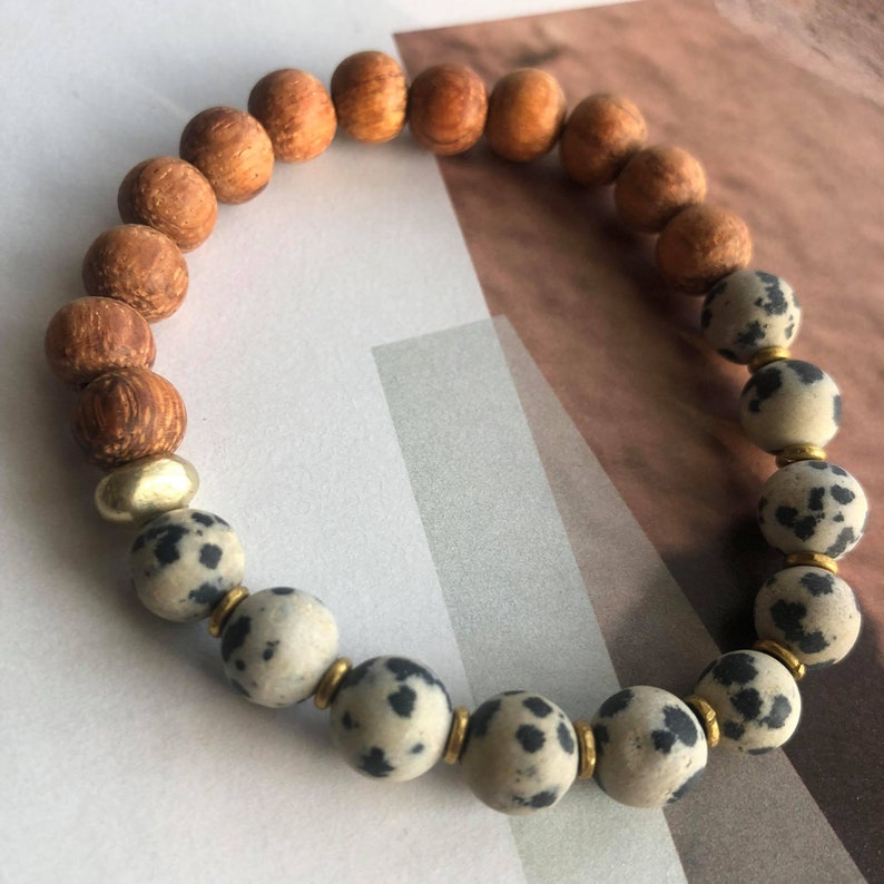 May include: A brown wooden beaded bracelet with a section of white and black speckled beads and gold spacers.