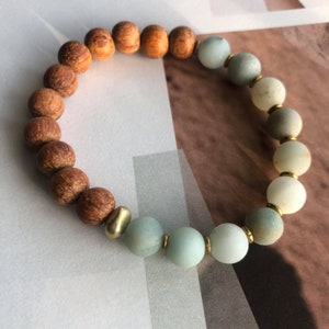 May include: A beaded bracelet with brown wooden beads and light green beads separated by gold spacers.