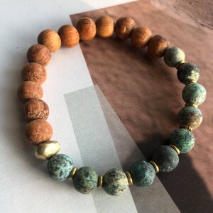 May include: A wooden and turquoise beaded bracelet with gold accents. The bracelet has a gradient of brown wood beads transitioning to turquoise beads.