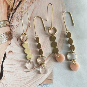 May include: Three pairs of gold dangle earrings with different charms. One pair has three gold circles and a clear glass circle. Another pair has three gold circles and a pink circle. The third pair has three gold circles and a clear glass circle.