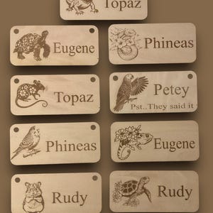 May include: A selection of wooden name tags, each engraved with an animal illustration and a name. The tags showcase a lizard, tortoise, rat, parrot, bird, hamster, and turtle. Each tag has a small hole at the top for hanging.