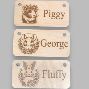 May include: Three wooden pet tags with engraved animal illustrations and names. The top tag features a guinea pig with the name "Piggy". The middle tag shows a chinchilla with the name "George". The bottom tag displays a rabbit with the name "Fluffy".