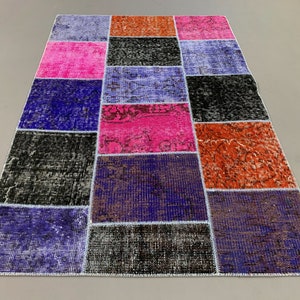 Puede incluir: Una alfombra de patchwork con cuadrados de diferentes colores, incluyendo rosa, azul, negro y naranja. La alfombra está hecha de tejido tejido y tiene un borde con flecos.