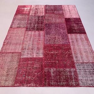 May include: A patchwork rug with a variety of shades of red and pink. The rug is made of different pieces of fabric that have been sewn together.