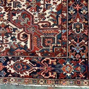 May include: Close-up of a traditional Persian rug with intricate patterns in shades of red, blue, and cream. The rug has a fringe border and is woven with a high knot count.