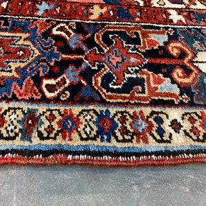 May include: Close-up of the bottom edge of a rug with a detailed, intricate pattern in shades of red, blue, and cream. The rug has a fringe border.