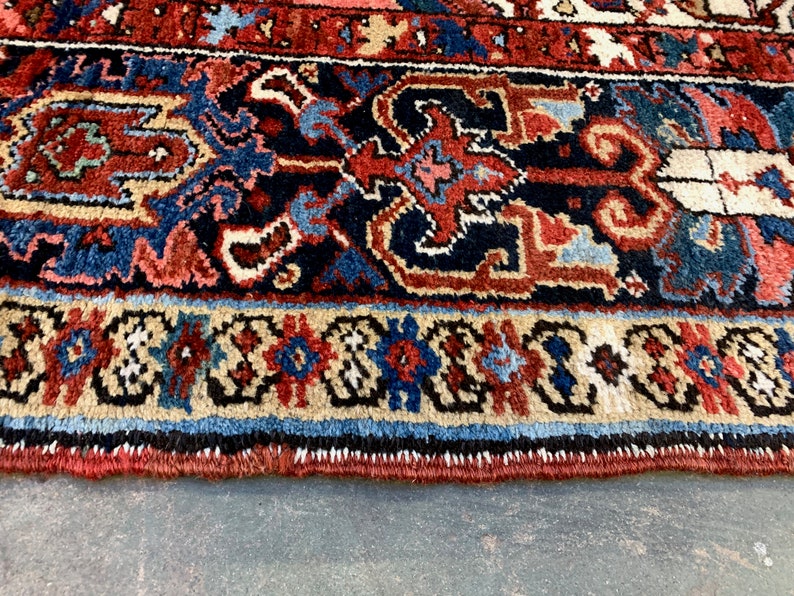 May include: Close-up of the bottom edge of a rug with a detailed, intricate pattern in shades of red, blue, and cream. The rug has a fringe border.