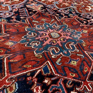 May include: A close-up of a traditional Persian rug with intricate patterns in shades of red, blue, and cream. The rug features a central medallion with a floral design and geometric borders.