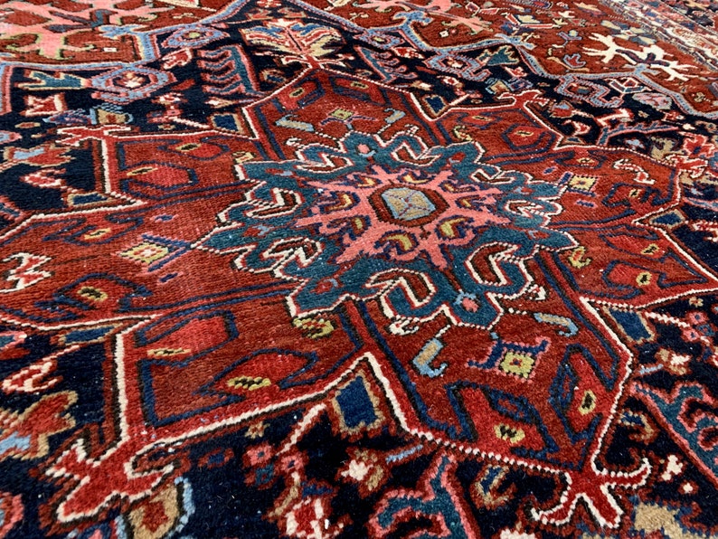 May include: A close-up of a traditional Persian rug with intricate patterns in shades of red, blue, and cream. The rug features a central medallion with a floral design and geometric borders.