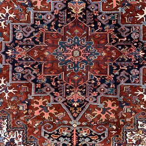 May include: A traditional Persian rug with a red background and intricate blue, white, and pink patterns. The rug features a central medallion with a starburst design.