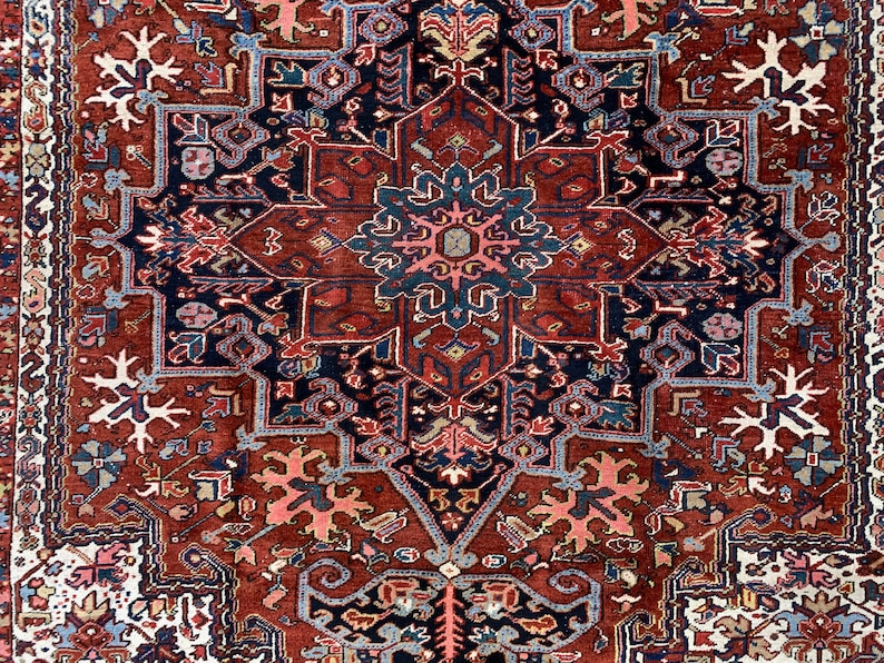 May include: A traditional Persian rug with a red background and intricate blue, white, and pink patterns. The rug features a central medallion with a starburst design.