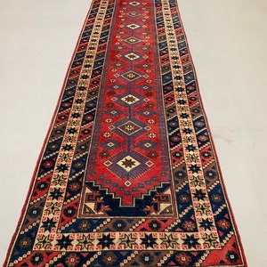 May include: A long, narrow red, blue, and cream colored rug with a geometric pattern. The rug has fringe on both ends.
