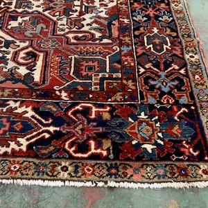 May include: A traditional Persian rug with a red, blue, and white geometric pattern. The rug has a fringe border and is made of wool.