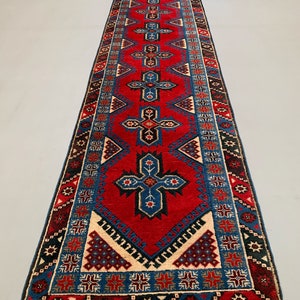 May include: A long, narrow red rug with a blue and white geometric pattern. The rug has a fringe on both ends.