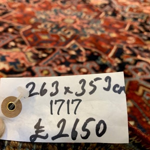 May include: A white tag with black writing on a red and blue patterned rug. The tag reads "263 x 353 cm 1717 &pound;2650".