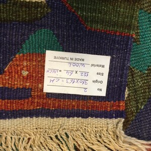 May include: A hand-woven wool rug with a geometric pattern in shades of blue, green, orange, and cream. The rug measures 122 x 64 inches and has a fringed edge. The tag indicates it was made in Turkiye.