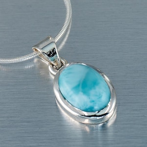 Op de afbeelding: Een zilveren hangerketting met een ovale, lichtblauwe edelsteen. De edelsteen is gezet in een zilveren bezel en hangt aan een fijne zilveren ketting. De hanger heeft een gepolijste afwerking en een eenvoudig, elegant ontwerp.