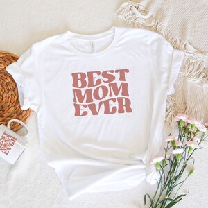 May include: White t-shirt with a pink retro-style graphic that says "Best Mom Ever".