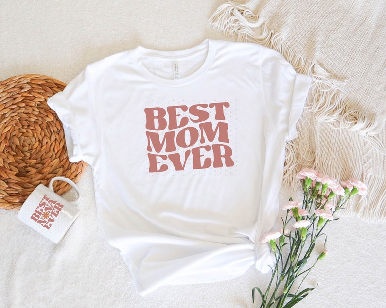 May include: White t-shirt with a pink retro-style graphic that says "Best Mom Ever".