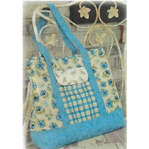 May include: A floral tote bag with a light blue base and straps. The bag features a cream-coloured fabric with blue flower patterns and a plaid pocket. The bag is sitting on a floral patterned surface.