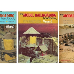 May include: Three softcover books titled The Model Railroading Handbook, Volumes I, II, and III by Robert Schleicher. Each cover features a colour photograph of a detailed model train layout, including tracks, locomotives, and miniature buildings.