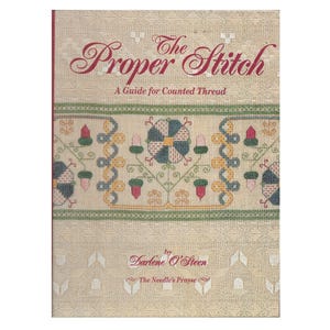 May include: A book titled "The Proper Stitch: A Guide for Counted Thread" with a beige cover. The title is in burgundy script, and the cover features a detailed cross-stitch design in green, blue, yellow, and red. The author's name is Darlene O'Steen.