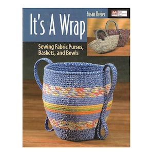 Puede incluir: Un libro titulado "It's A Wrap" de Susan Breier, que presenta una cesta de tela azul y amarilla con asas y el texto "Sewing Fabric Purses, Baskets, and Bowls".