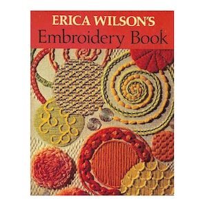 May include: The cover of "Erica Wilson's Embroidery Book" features a red banner with the title in white. The book's cover showcases various embroidery designs in shades of orange, yellow, and green, including circular and spiral patterns.