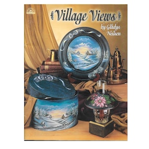 May include: A book titled "Village Views" by Gladys Neilson, featuring painted winter scenes on a round plate, a round box, and a lampshade. The book cover is a warm brown color with a gold-colored curtain in the background.