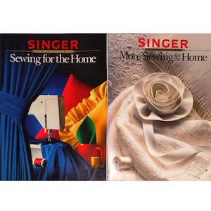 Könnte beinhalten: Zwei Vintage Singer Nähbücher, "Sewing for the Home" und "More Sewing for the Home". Das erste Buch zeigt eine Nähmaschine, blauen Stoff und bunte Kissen. Das zweite Buch zeigt eine weiße Stoffrose und eine Garnrolle.