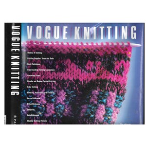 May include: A close-up of a knitting project in progress, with needles holding a vibrant, multi-colored knitted fabric. The book "VOGUE KNITTING" is visible, with a list of topics including "History of Knitting" and "Color Knitting".