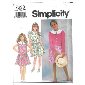 Può includere: Cartamodello Simplicity 7693, taglia AA (7-10), con illustrazioni di tre completi: un vestito rosa a pois con colletto bianco, un vestito a fiori a maniche corte e una giacca rosa a maniche lunghe indossata sopra una gonna a fiori.