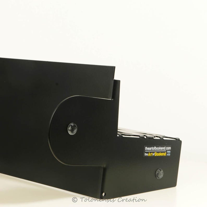 May include: Black metal bookend with a unique design. The bookend has a curved shape and a small metal screw on the side. The bookend is labeled "the Art of Bookend".