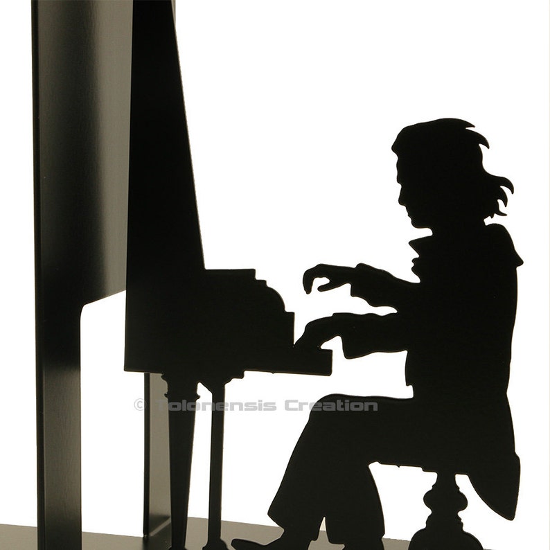 May include: Black metal bookend featuring a silhouette of a person playing a piano. The bookend is a decorative piece for a home or office.