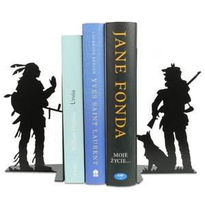 Op de afbeelding: Zwarte metalen boekenleggers met een silhouet van een indiaan aan de linkerkant en een silhouet van een persoon met een hond aan de rechterkant. De boekenleggers houden drie boeken vast met de titels "William Ospina", "Ursula", "Yves Saint Laurent" en "Jane Fonda - Moje Zycie..."
