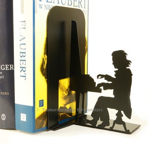 May include: Black metal bookends shaped like a person playing a piano. The bookends are a silhouette of a person sitting at a piano with their hands on the keys. The bookends are a modern and stylish way to hold your books.