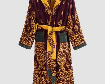 Puede incluir: Una bata larga de color burdeos con capucha, con un estampado paisley dorado y burdeos. La bata tiene un cinturón y bolsillos a juego.
