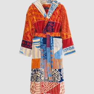 Pode incluir: Uma bata de banho colorida em patchwork com capuz. A bata é feita de um material macio e absorvente e apresenta uma variedade de padrões florais e geométricos em tons de vermelho, azul, laranja e creme.