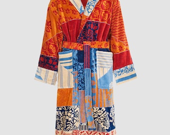 Puede incluir: Una bata de baño de patchwork colorida con capucha. La bata está hecha de un material suave y absorbente y presenta una variedad de patrones florales y geométricos en tonos rojos, azules, naranjas y crema.