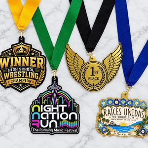 May include: Four medals with ribbons: a black and gold shield-shaped wrestling medal, a black shield-shaped Night Nation Run medal, a gold circular medal with wings, and a rectangular Raíces Unidas medal with blue flowers and a beach scene.