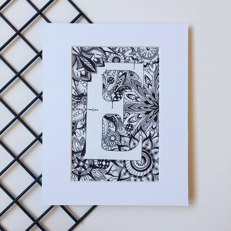 May include: A black and white drawing of the letter "E" surrounded by intricate floral patterns. The letter is outlined in white and the background is filled with detailed designs.