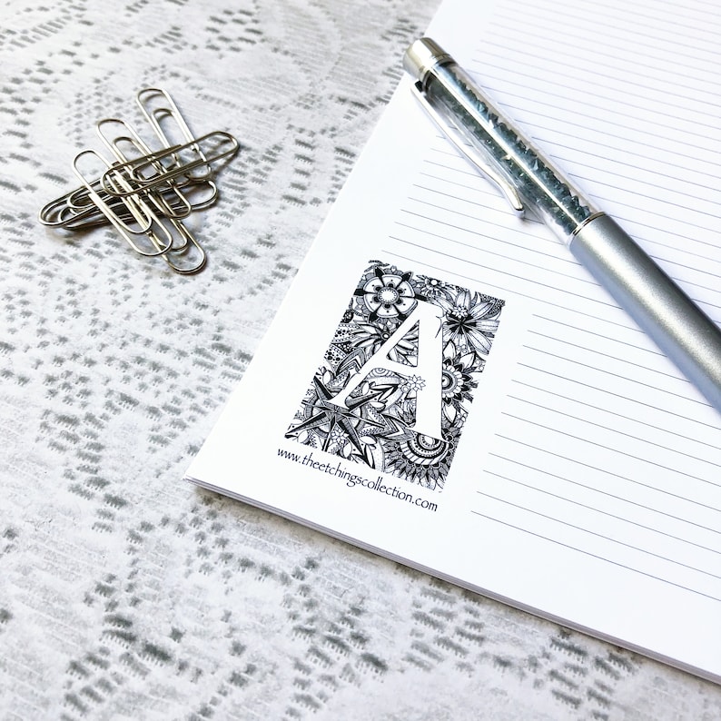 May include: A black and white illustration of the letter A surrounded by floral and nautical designs. The illustration is on a white notepad with lined paper. The text "www.theetchingscollection.com" is printed below the illustration.