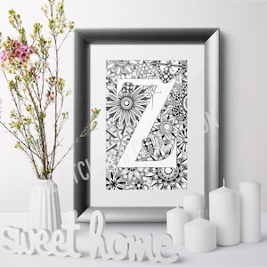 May include: A black and white framed print of the letter Z surrounded by intricate floral designs. The print is displayed on a white surface with candles and a white sign that reads "sweet home".