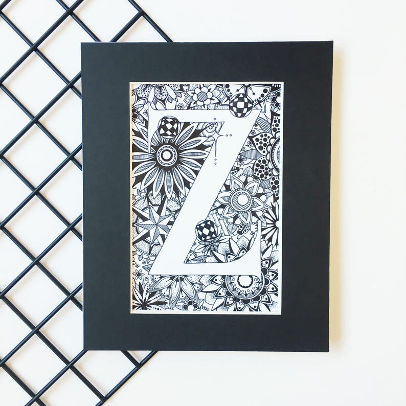 May include: A black and white framed print of the letter Z surrounded by intricate floral and geometric patterns.