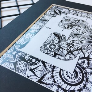 May include: Black and white framed art print featuring a stylized letter 'F' with intricate floral and geometric patterns.