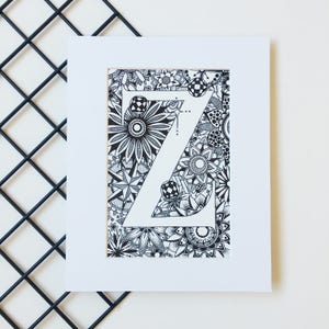 May include: A black and white illustration of the letter Z surrounded by intricate floral designs. The letter is outlined in white and the background is filled with black and white flowers, leaves, and swirls.